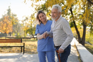 Photo of Caregiver assisting senior man in park. Home health care service