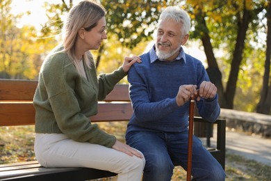 Caregiver assisting senior man on wooden bench in park. Home health care service