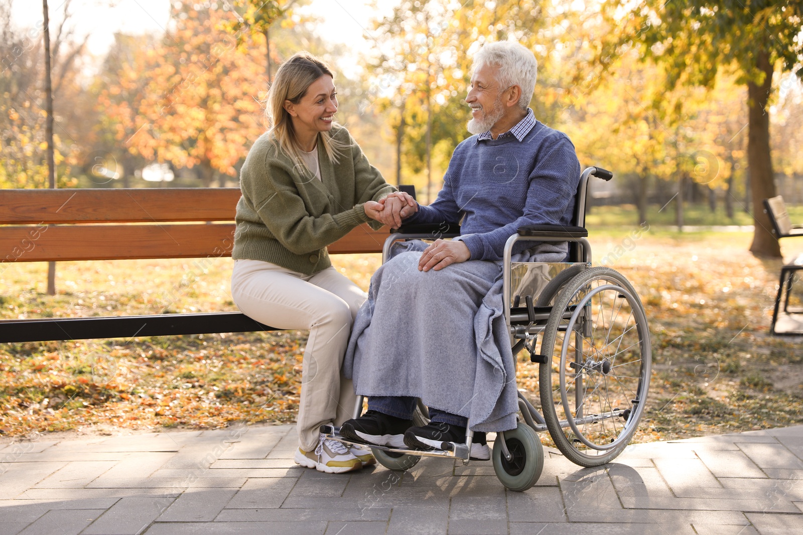 Photo of Caregiver assisting senior man on wheelchair in park. Home health care service