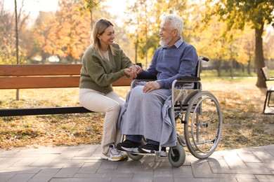 Photo of Caregiver assisting senior man on wheelchair in park. Home health care service