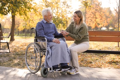 Photo of Caregiver assisting senior man on wheelchair in park. Home health care service