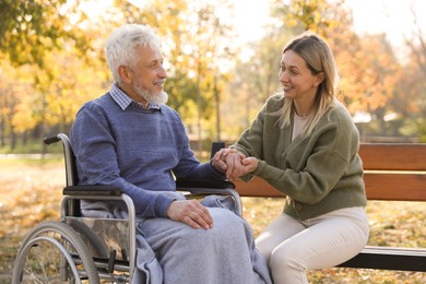 Photo of Caregiver assisting senior man on wheelchair in park. Home health care service