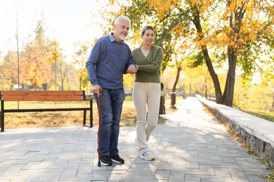 Photo of Caregiver assisting senior man in park. Home health care service