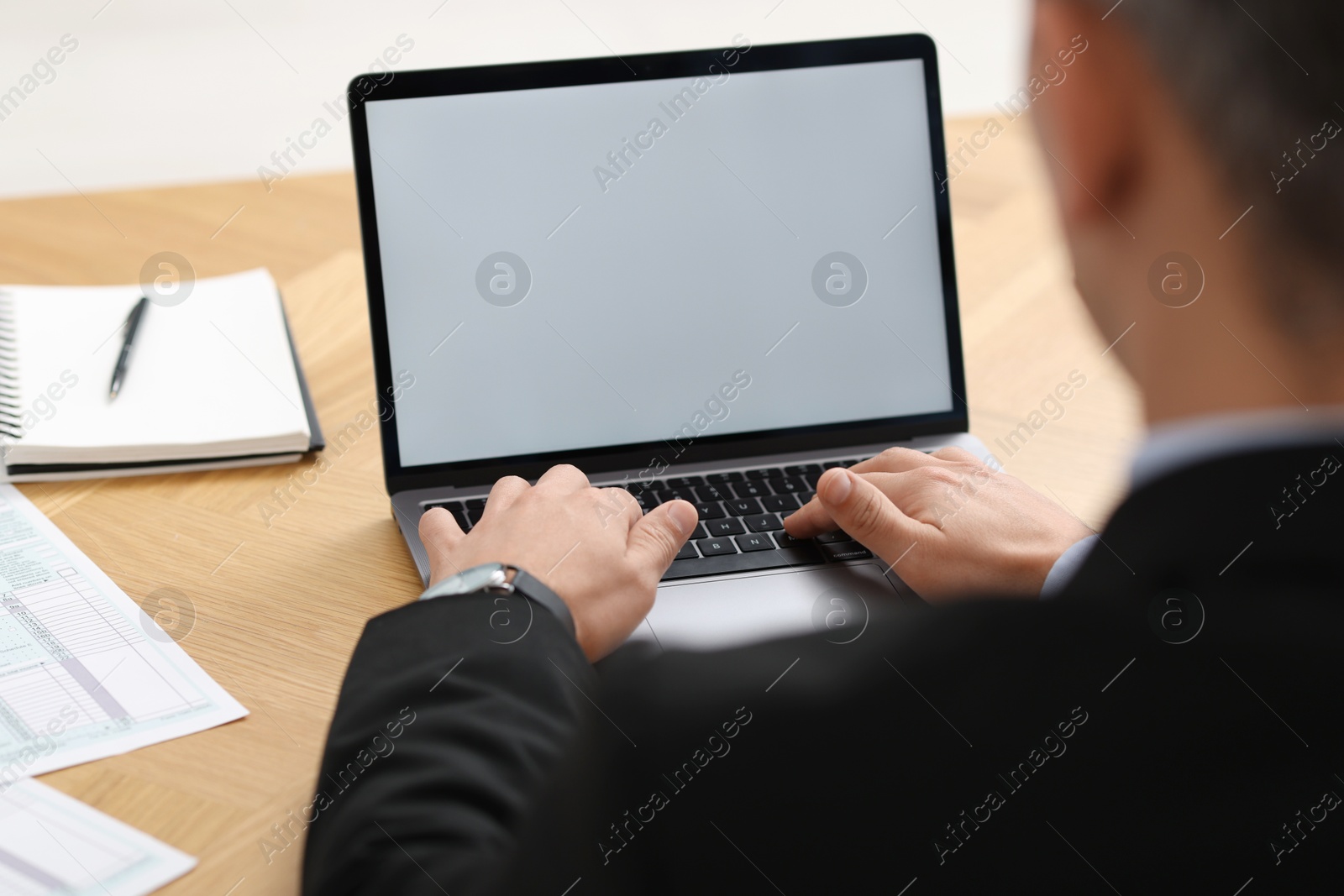 Photo of Businessman working with laptop at wooden table in office, closeup