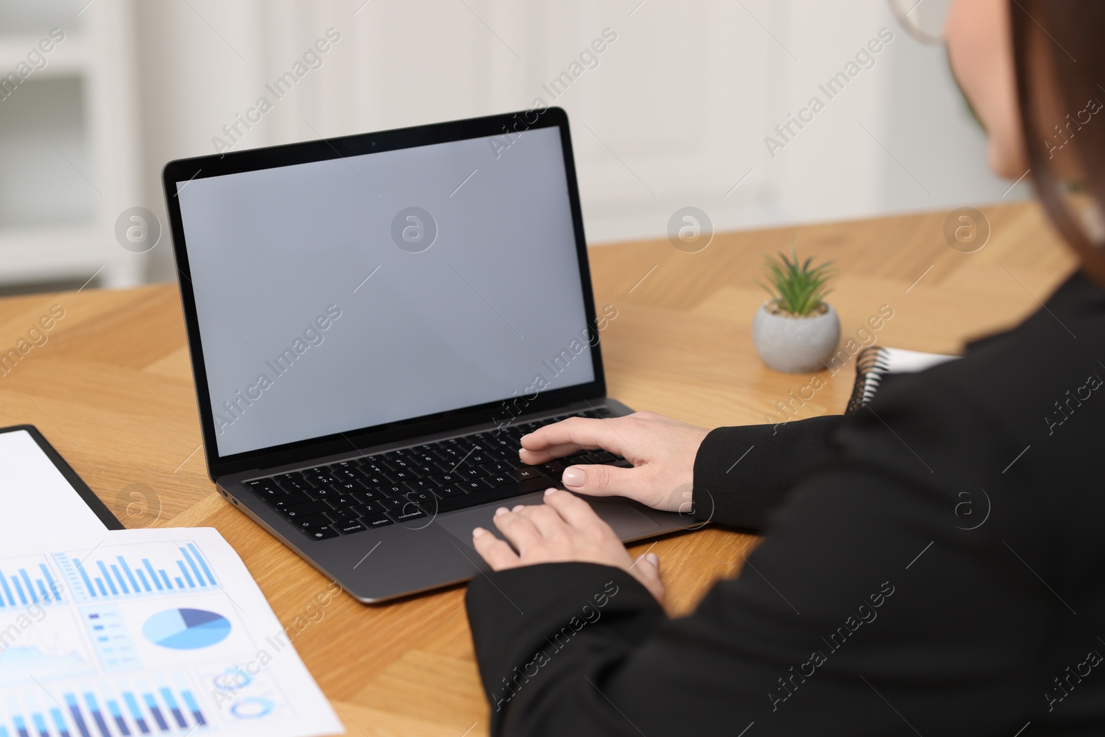 Photo of Businesswoman working with laptop at wooden table in office, closeup