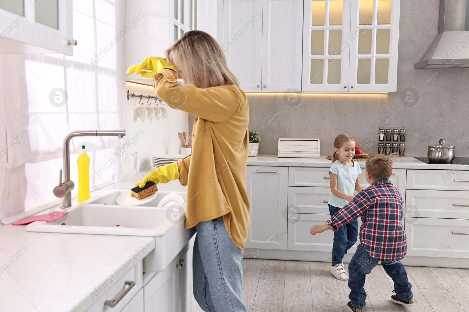 Photo of Tired housewife washing dishes while her kids playing in kitchen