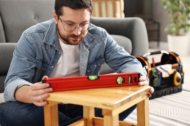 Photo of Man using level tool while repairing wooden stool at home