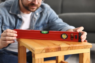 Photo of Man using level tool while repairing wooden stool at home, closeup