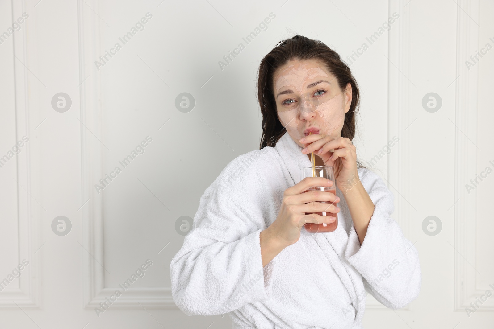 Photo of Spa day. Beautiful woman with face mask drinking juice indoors, space for text