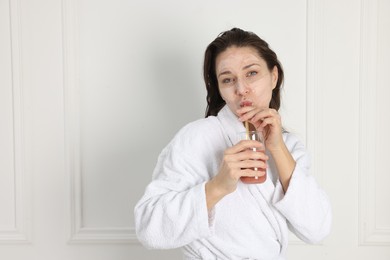 Photo of Spa day. Beautiful woman with face mask drinking juice indoors, space for text