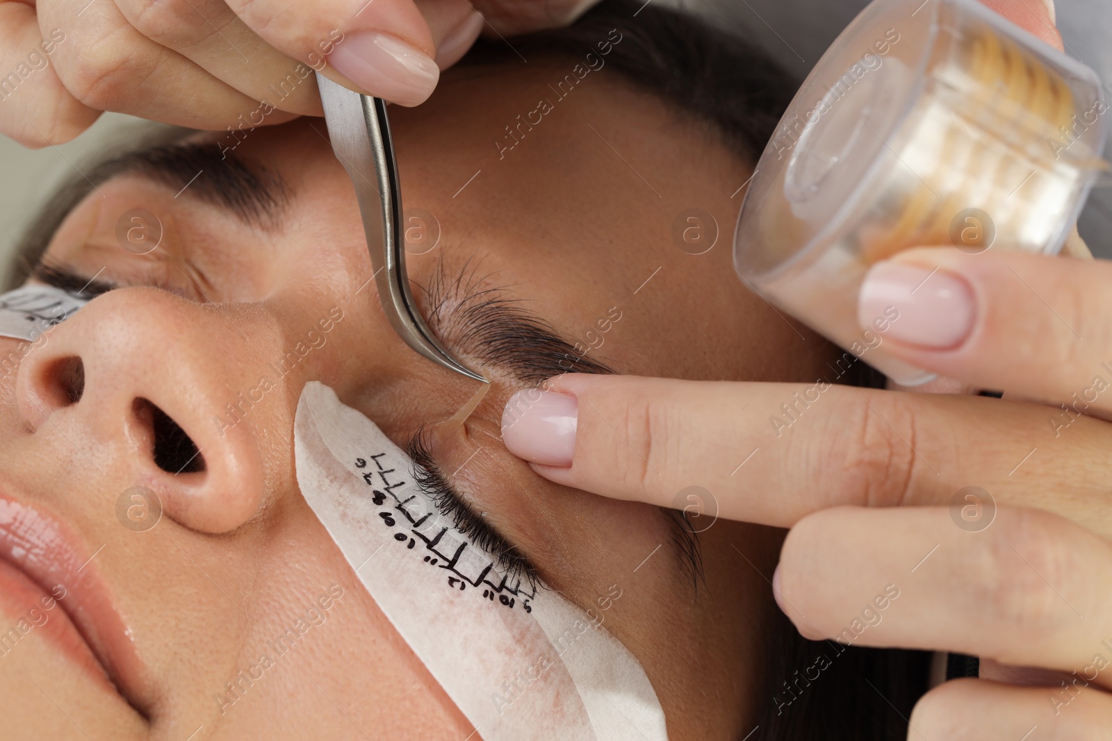 Photo of Esthetician taping woman's eyelid before lash extensions procedure in beauty salon, closeup