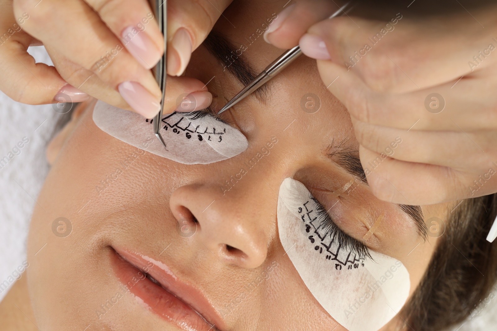 Photo of Woman undergoing lash extensions procedure in beauty salon, closeup