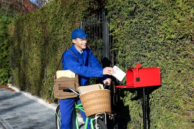 Photo of Postman with bicycle putting parcel into mail box outdoors