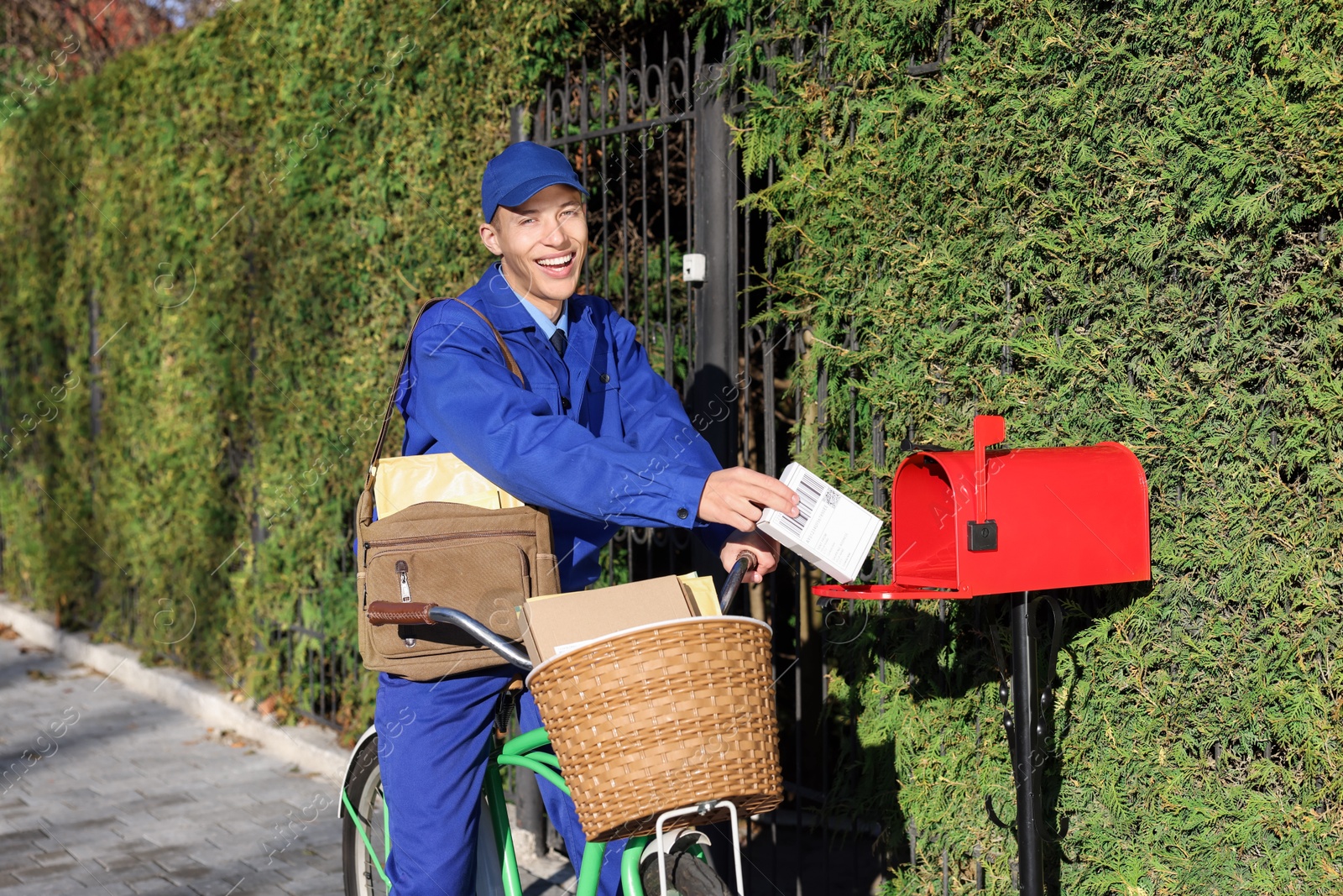 Photo of Postman with bicycle putting parcel into mail box outdoors