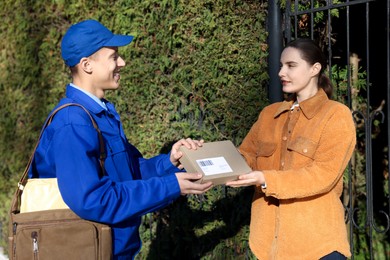 Photo of Woman receiving parcel from postman outdoors. Mail service