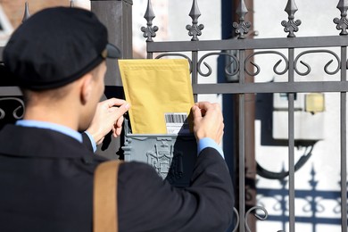 Postman putting envelope into mail box outdoors