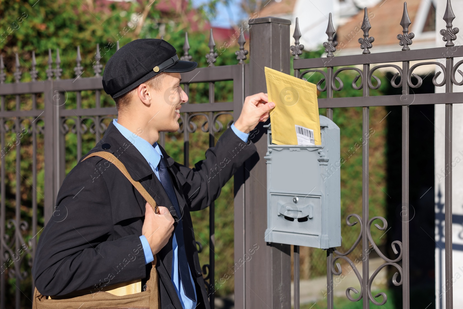 Photo of Happy postman putting envelope into mail box outdoors