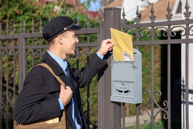 Happy postman putting envelope into mail box outdoors