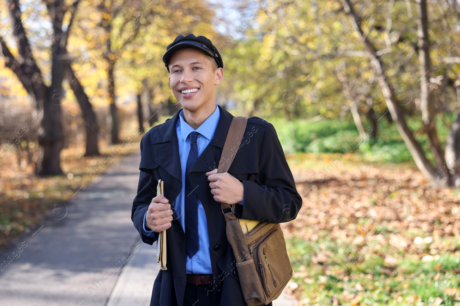 Photo of Happy postman with bag and envelopes outdoors