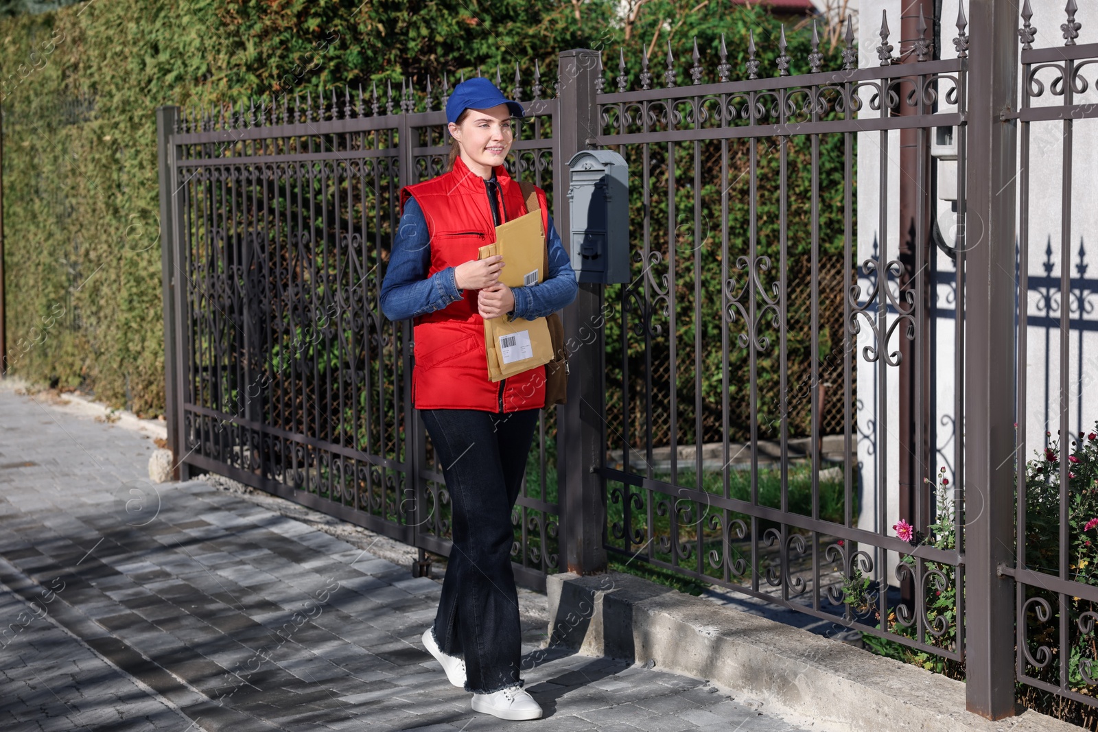 Photo of Mailwoman in uniform with envelopes outdoors. Postal service