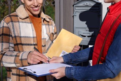 Man signing papers while receiving parcel from postwoman outdoors, closeup