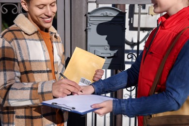 Man signing papers while receiving parcel from postwoman outdoors, closeup