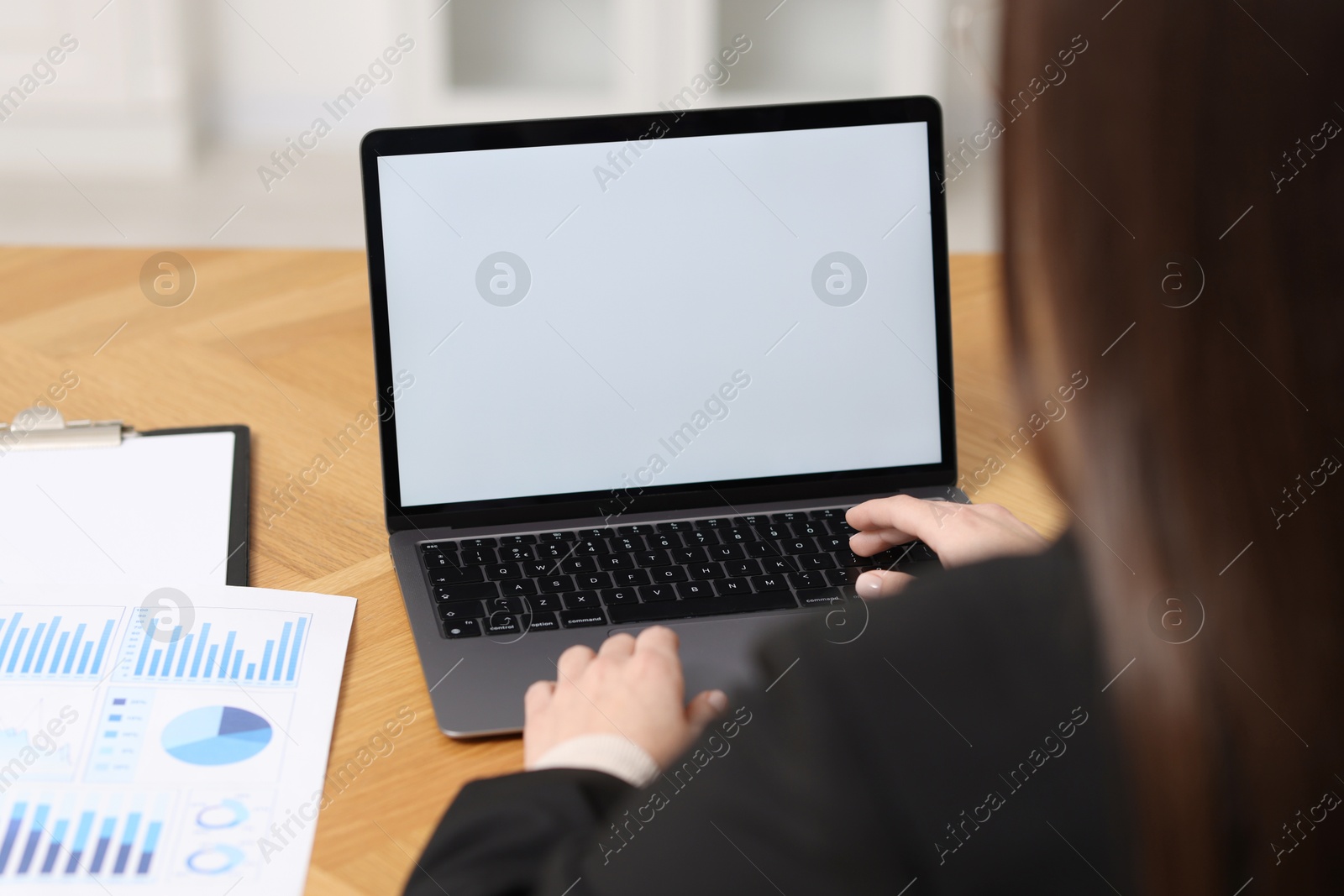 Photo of Businesswoman working with laptop at wooden table in office, closeup