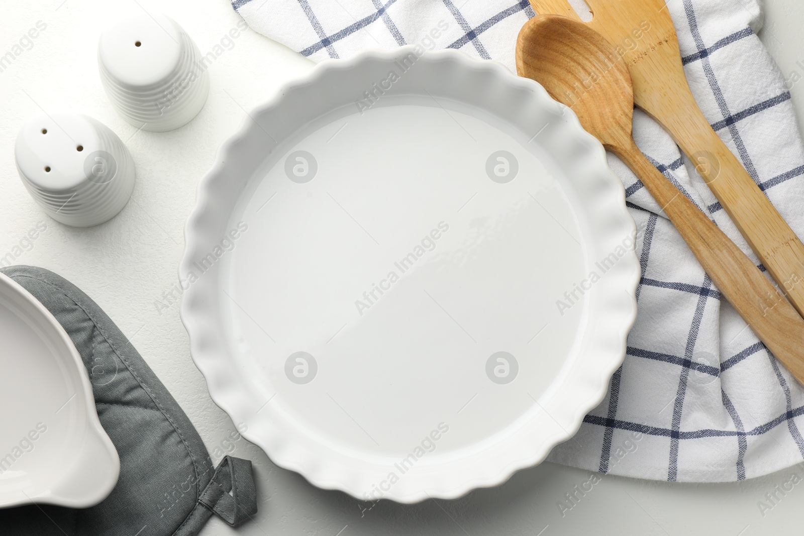 Photo of Ceramic casserole and other cooking utensils on white table, flat lay