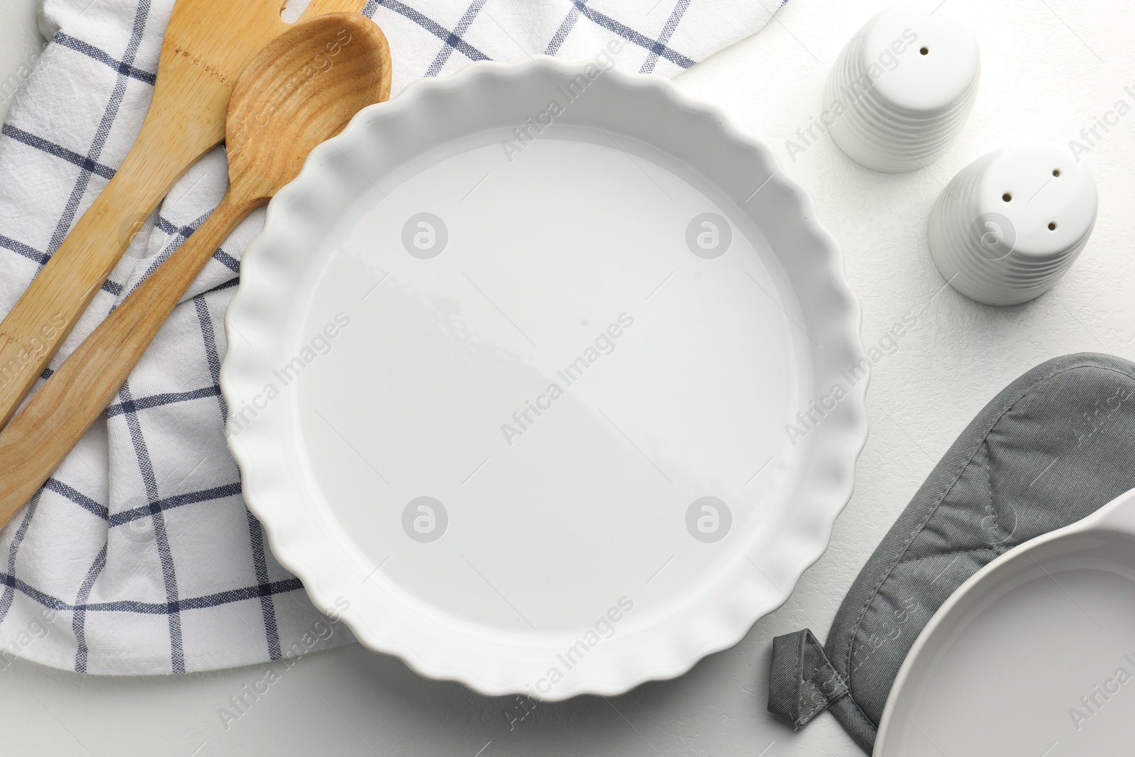 Photo of Ceramic casserole and other cooking utensils on white table, flat lay