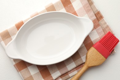 Photo of Ceramic casserole and brush on white table, top view