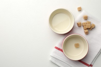 Photo of Ceramic casseroles and sugar cubes on white table, flat lay. Space for text