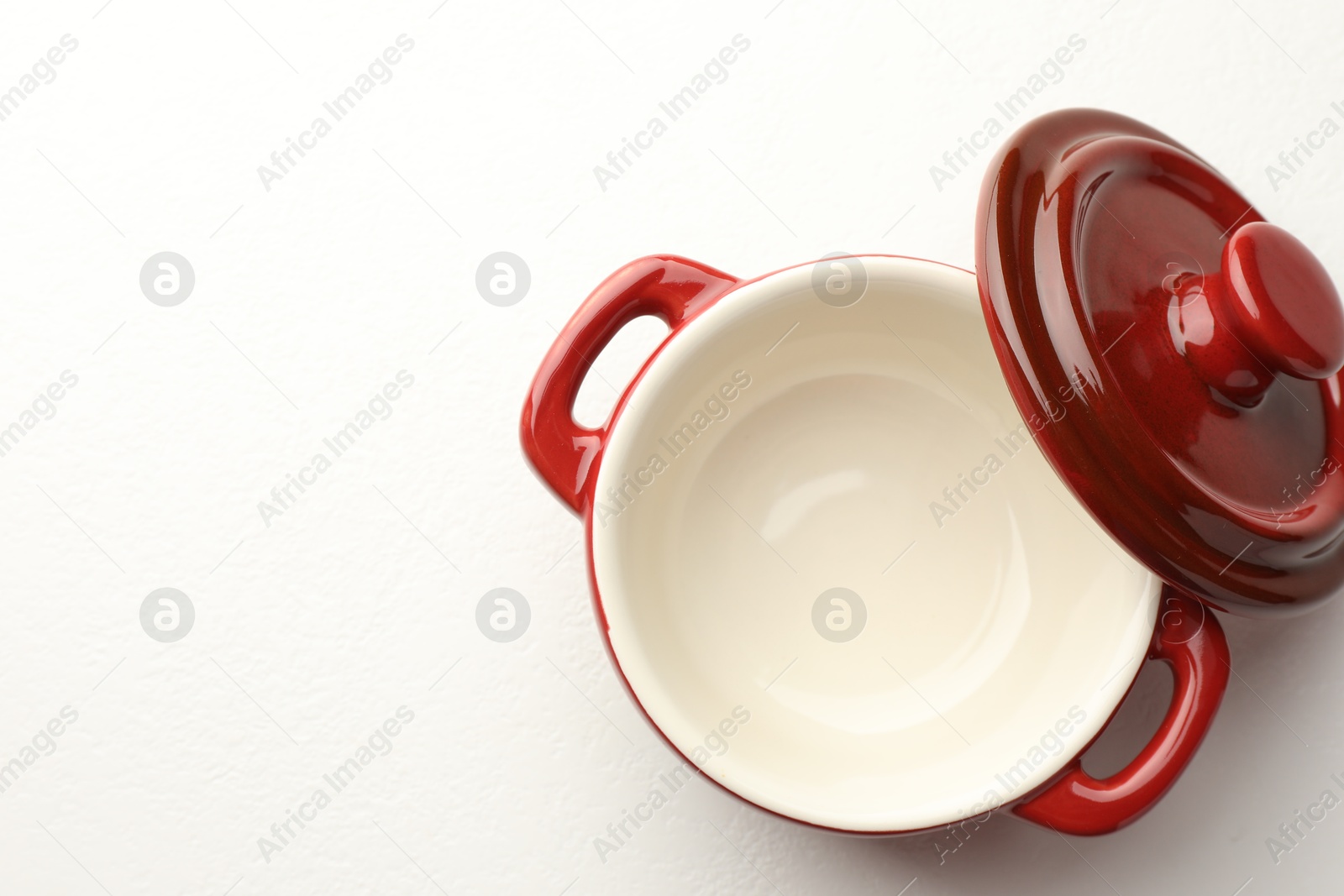 Photo of Ceramic casserole and lid on white table, top view. Space for text