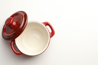 Photo of Ceramic casserole and lid on white table, top view. Space for text