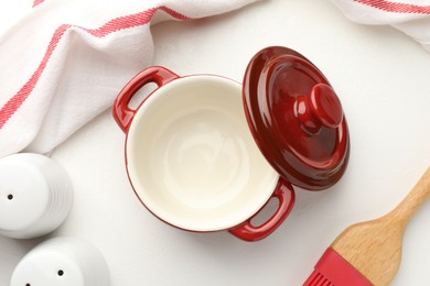 Photo of Ceramic casserole, lid, shakers and brush on white table, flat lay