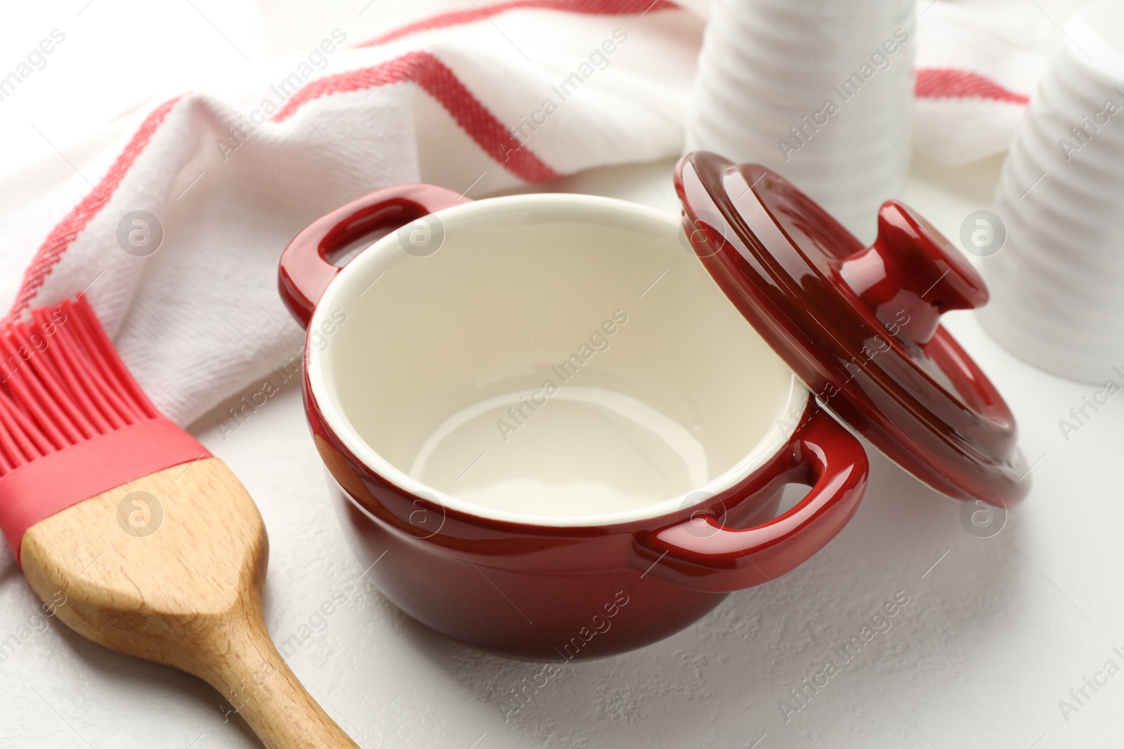 Photo of Ceramic casserole, lid, shakers and brush on white table, closeup