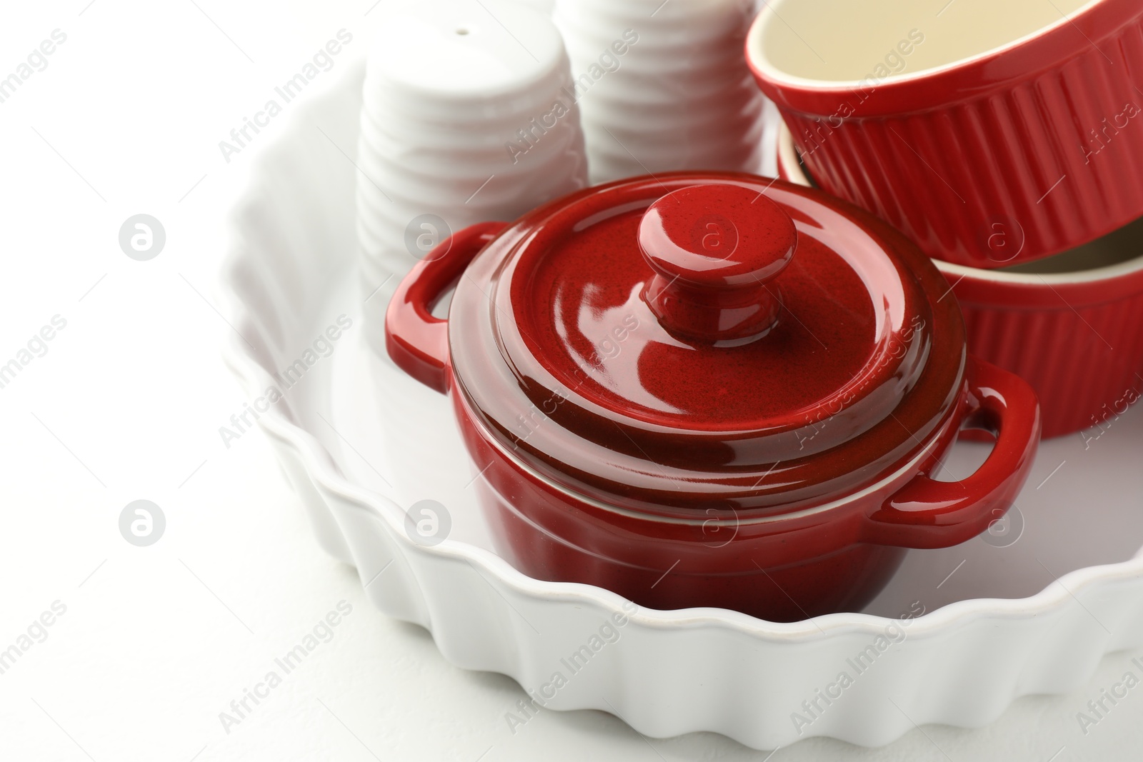 Photo of Different ceramic casseroles and shakers on white table, closeup