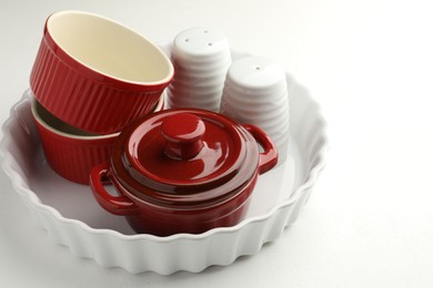 Photo of Different ceramic casseroles and shakers on white table, closeup