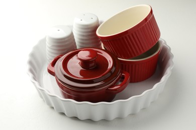 Photo of Different ceramic casseroles and shakers on white table, closeup