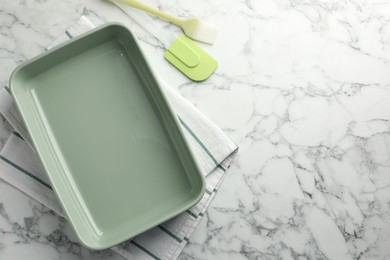 Photo of Ceramic casserole, spatula and brush on white marble table, flat lay. Space for text