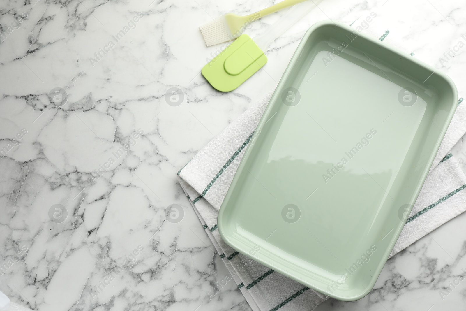 Photo of Ceramic casserole, spatula and brush on white marble table, flat lay. Space for text