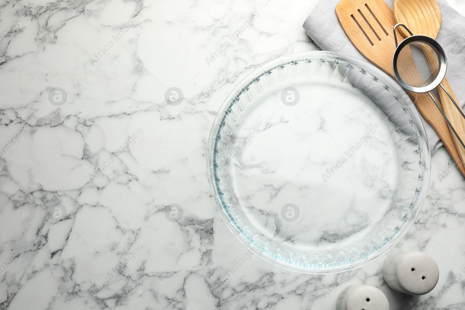 Photo of Glass casserole and other cooking utensils on white marble table, flat lay. Space for text