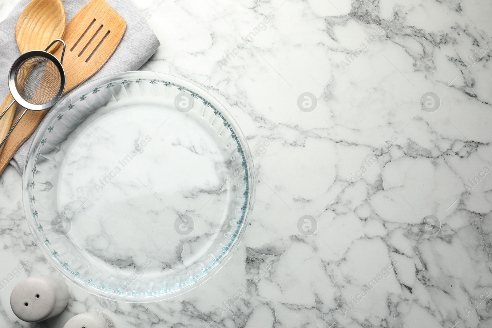 Photo of Glass casserole and other cooking utensils on white marble table, flat lay. Space for text