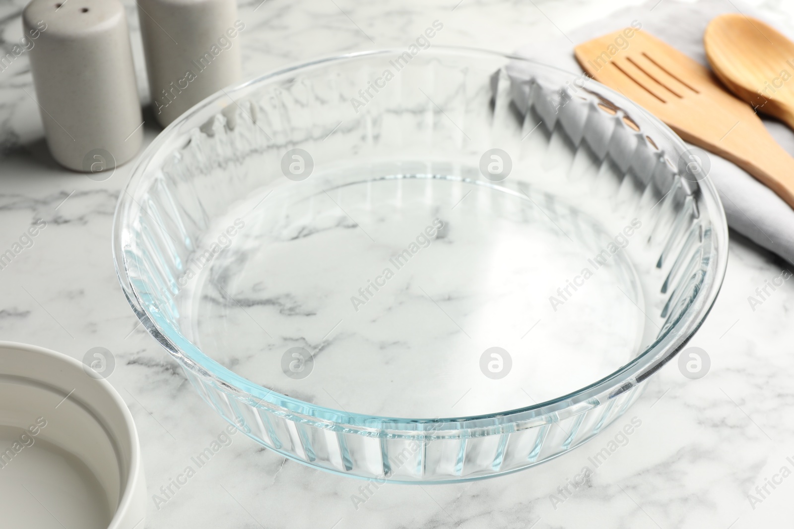 Photo of Glass casserole and other cooking utensils on white marble table, closeup