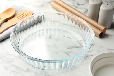 Photo of Glass casserole and other cooking utensils on white marble table, closeup