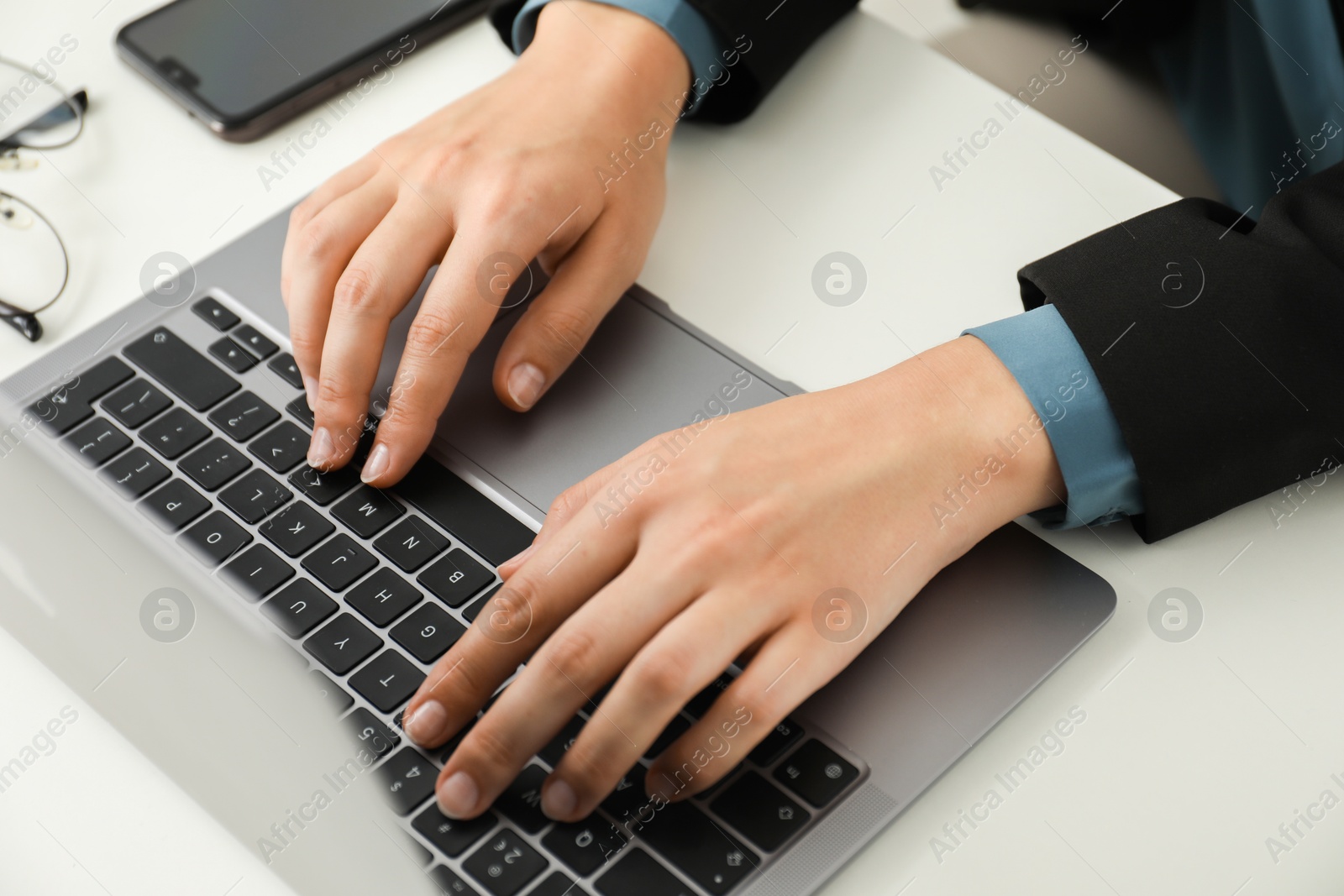 Photo of Businesswoman using laptop at white table indoors, closeup. Modern technology