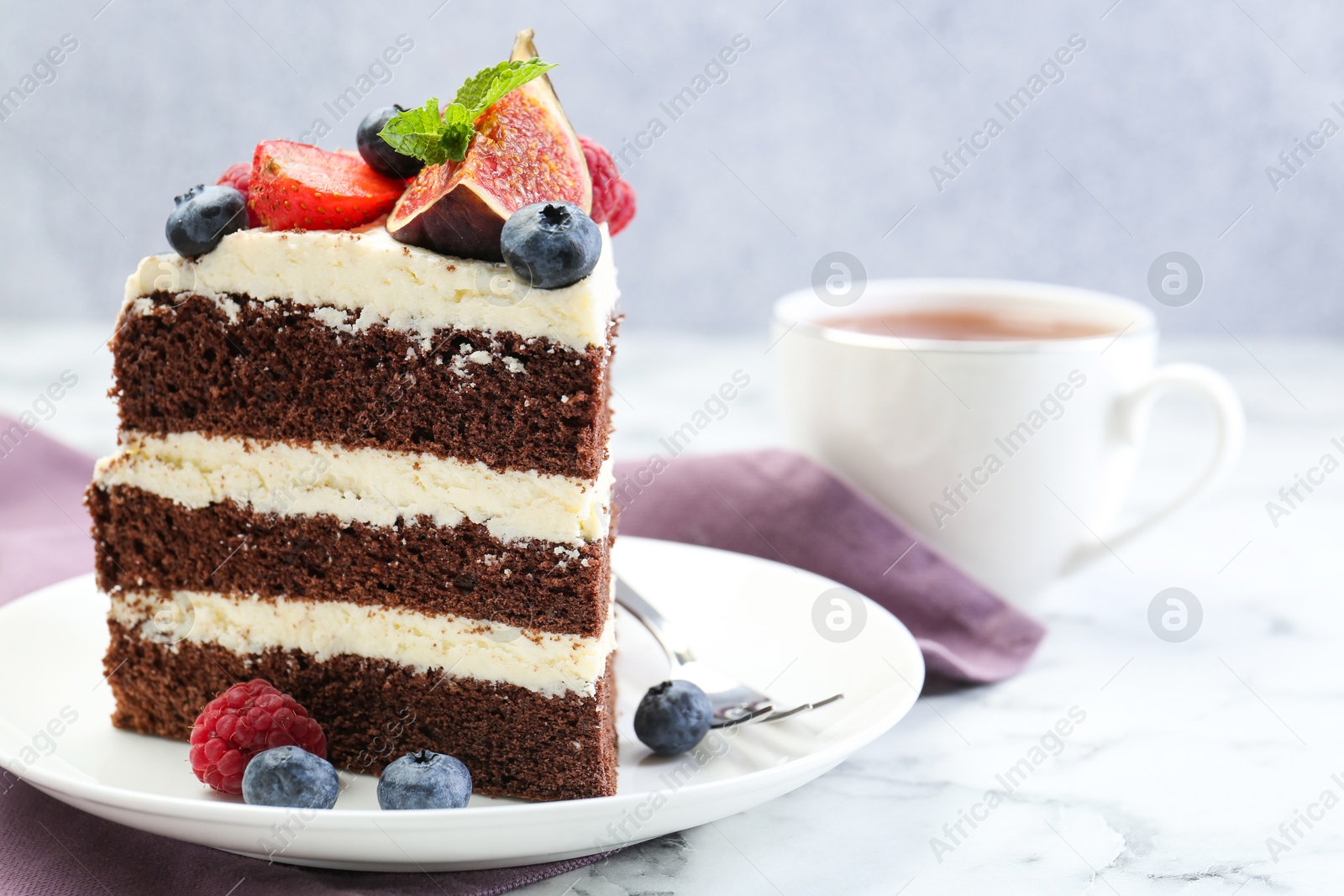 Photo of Piece of delicious chocolate sponge cake with berries and tea on white table, closeup