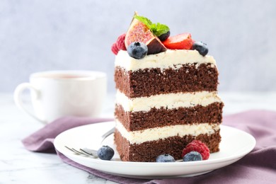 Photo of Piece of delicious chocolate sponge cake with berries and tea on white table, closeup