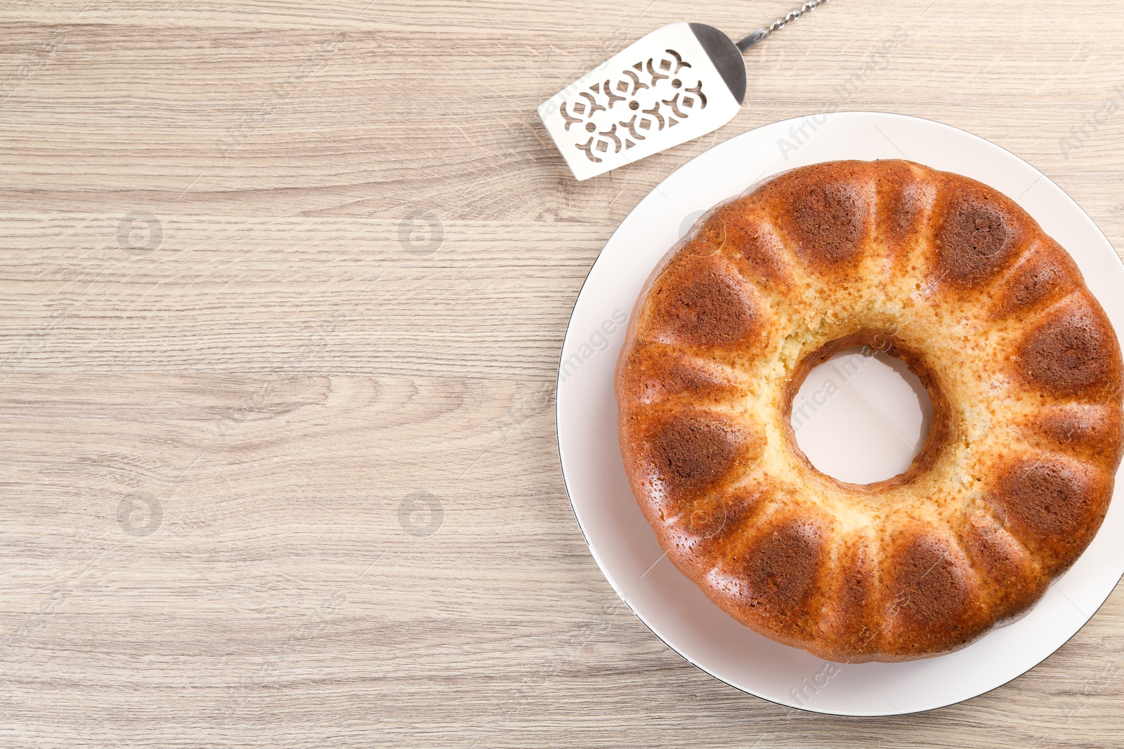 Photo of Freshly baked sponge cake and server on wooden table, top view. Space for text