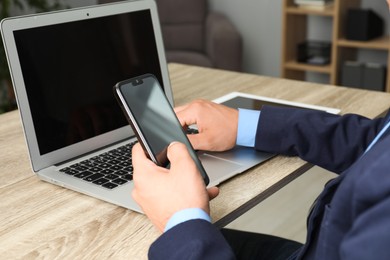 Photo of Businessman using smartphone and laptop at wooden table, closeup. Modern technology