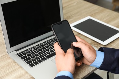 Photo of Businessman using smartphone near laptop at wooden table, closeup. Modern technology